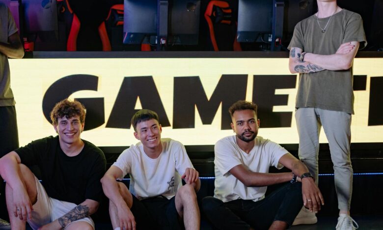Four young men posing confidently in an eSports arena with gaming setups in the background.