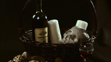 A dark-themed still life featuring a wine bottle, skull, candles, and a basket.