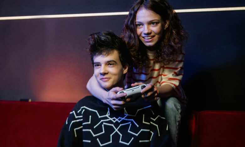 Two young adults having fun playing video games on a couch, smiling and holding a game controller.