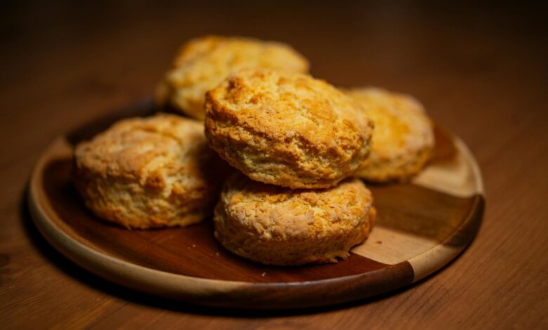 Freshly baked golden biscuits stacked on a wooden plate, perfect for breakfast or tea time.