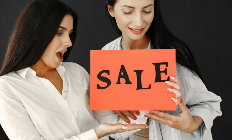 Two women energetically holding a 'SALE' sign, showcasing excitement and enthusiasm for a shopping event.