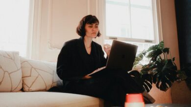 Woman in suit using laptop on sofa in bright room, modern lifestyle.