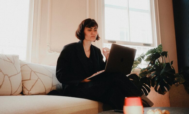Woman in suit using laptop on sofa in bright room, modern lifestyle.