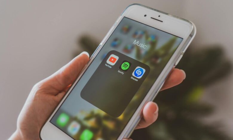 Hand holding a smartphone displaying popular music apps like Spotify and Shazam in a close-up shot.
