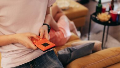 Person playing handheld game on couch, surrounded by relaxed setting with snacks.