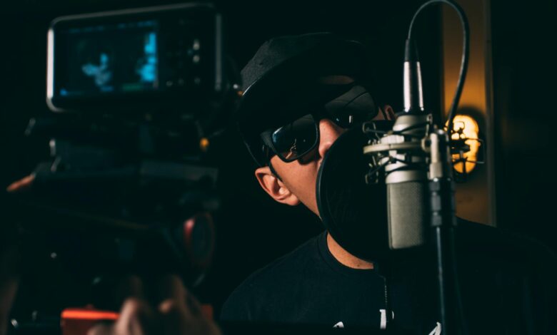 A hip-hop artist records vocals in a dark, atmospheric studio setting.