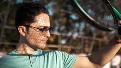 Young man in sunglasses holding a tennis racket outdoors on a sunny day.