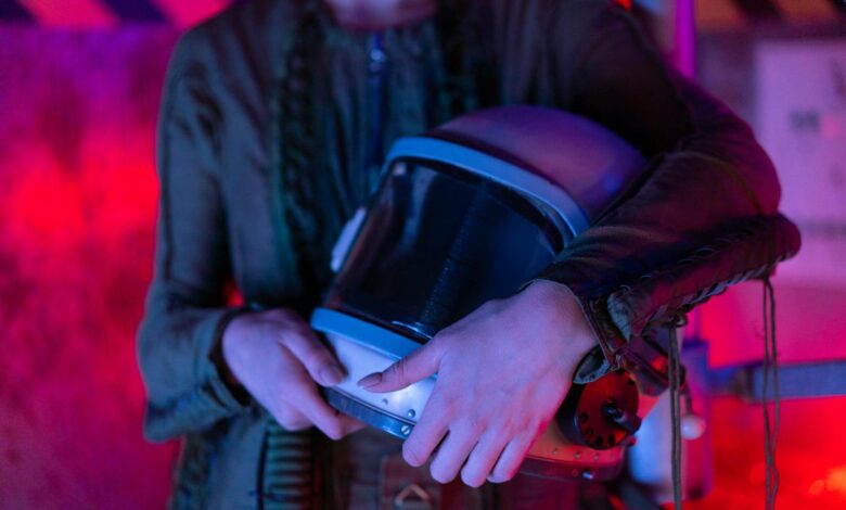 A person holding an astronaut helmet with neon lighting in a sci-fi setting.