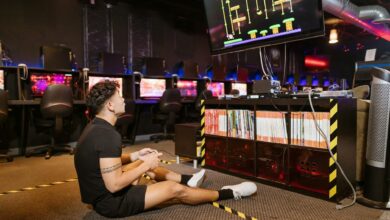 Man sitting on floor intensely playing video game at a modern arcade with vibrant computing equipment.