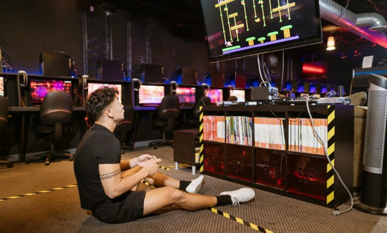 Man sitting on floor intensely playing video game at a modern arcade with vibrant computing equipment.