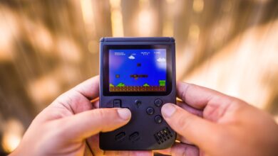 A close-up of hands holding a retro game console playing a classic Mario game outdoors.