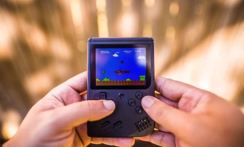 A close-up of hands holding a retro game console playing a classic Mario game outdoors.