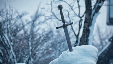 Close-up of a medieval sword embedded in snowy ground during winter.