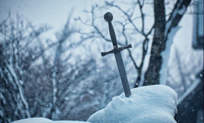 Close-up of a medieval sword embedded in snowy ground during winter.