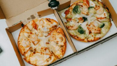 Two tasty shrimp pizzas with vegetables in delivery boxes on a table.