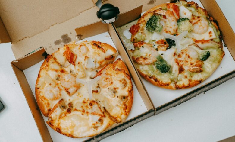 Two tasty shrimp pizzas with vegetables in delivery boxes on a table.