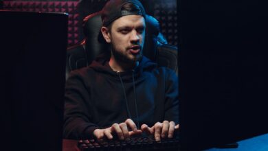 Man wearing cap typing on keyboard in a dimly lit room, concentrating on screen.