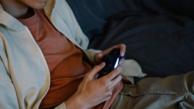 Crop anonymous man with console controller playing video game while sitting on couch in house