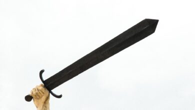A stone sculpture hand holding a large sword against a bright sky, symbolizing power and strength.