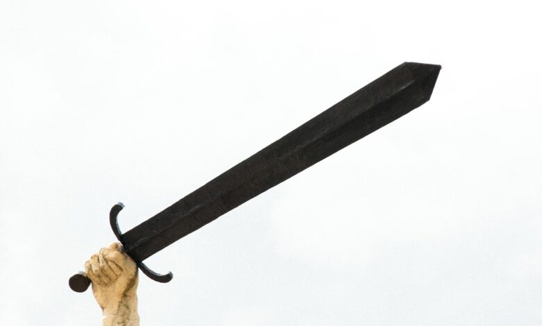 A stone sculpture hand holding a large sword against a bright sky, symbolizing power and strength.