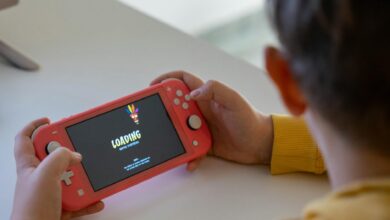 Child holding a pink handheld game console while a digital game loads on the screen.