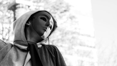 Black and white photo of a person wearing a mask and hoodie, evoking mystery.
