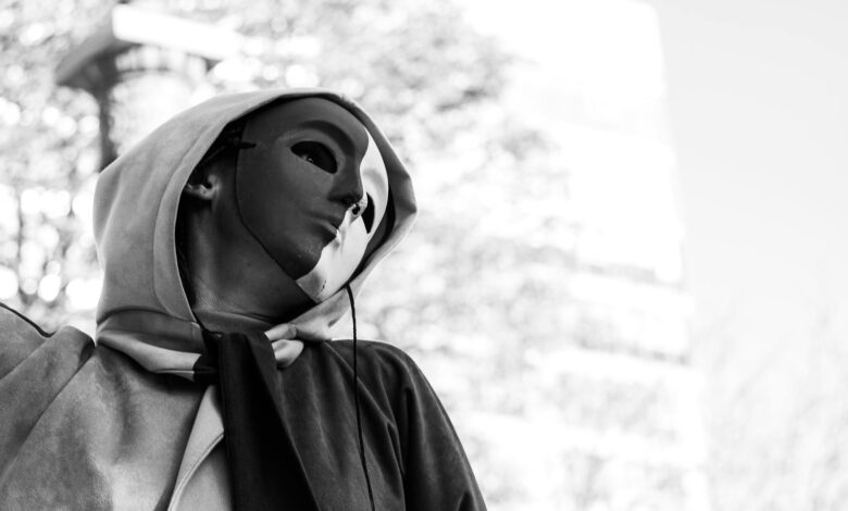 Black and white photo of a person wearing a mask and hoodie, evoking mystery.