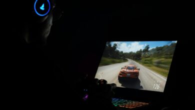 A gamer using a laptop and headphones to play a car racing game in a dark setting.
