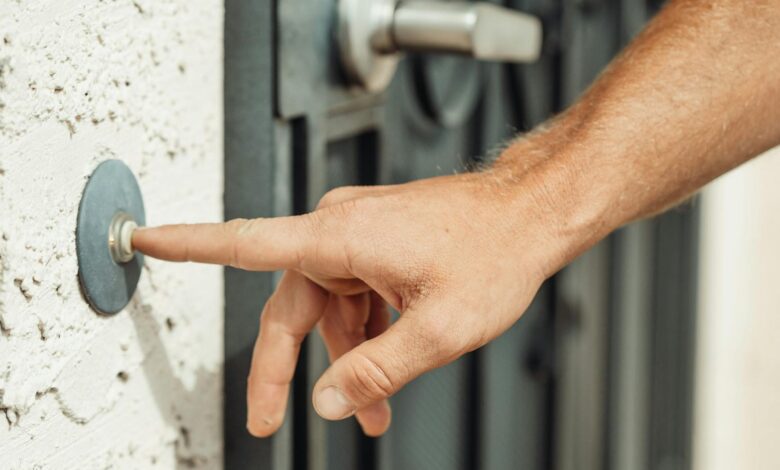 A close-up image of a hand pressing a doorbell outside a modern residential door.