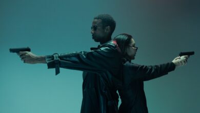 Two adults back-to-back, holding handguns, in a conceptual cyberpunk-like setting with cool tones.