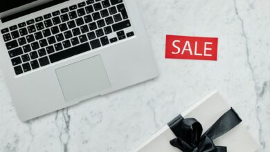 Top-down view of a laptop and gift with a sale sign on marble background.