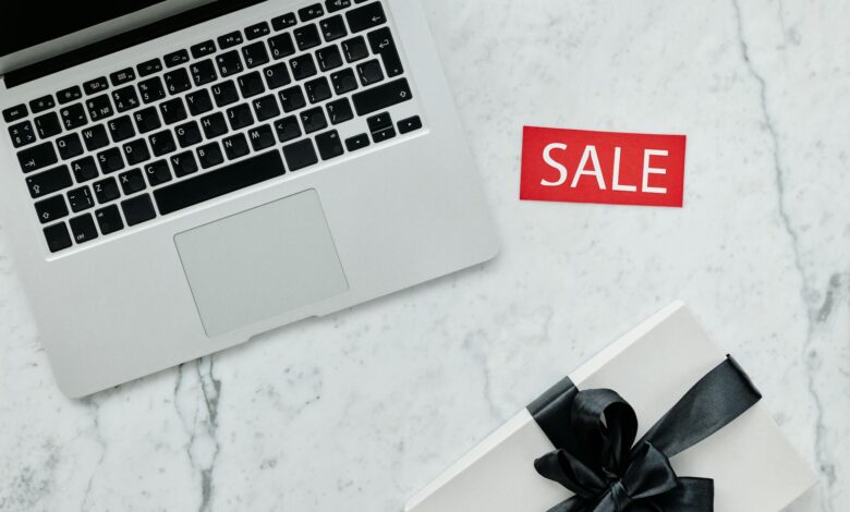 Top-down view of a laptop and gift with a sale sign on marble background.
