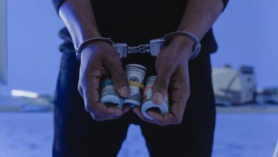 Close-up of handcuffed hands holding rolled cash, suggesting crime or arrest.