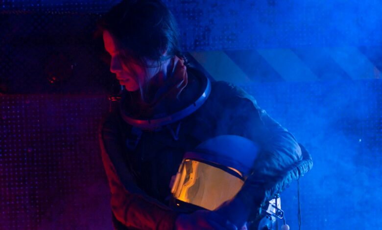 A futuristic portrait of a female astronaut holding her helmet in a dramatic blue light setting.
