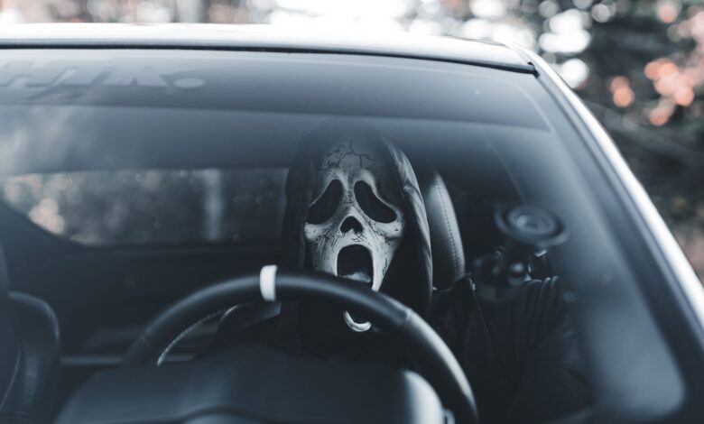 Masked individual in car adds an eerie vibe, suitable for Halloween themes.