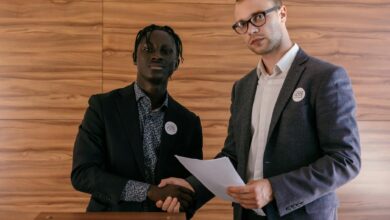 Two men in business attire shaking hands with agreement, promoting voting indoors.