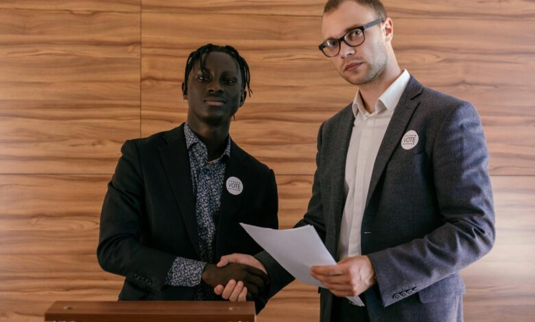 Two men in business attire shaking hands with agreement, promoting voting indoors.