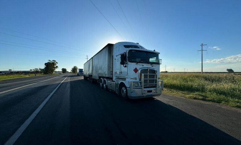 A silver semi truck driving on an open highway under a clear blue sky.