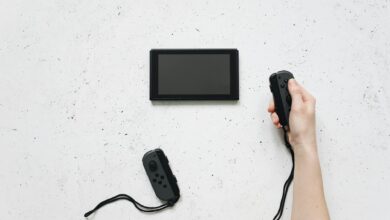 A person holds a Joy-Con controller with a Nintendo Switch on a white textured surface.