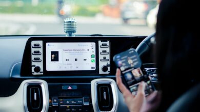 Car dashboard with a touchscreen display and person using a smartphone inside a vehicle.