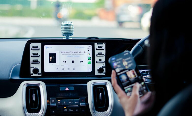 Car dashboard with a touchscreen display and person using a smartphone inside a vehicle.