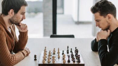Two adults deeply engaged in a strategic chess match on a wooden table indoors.