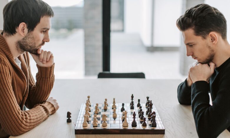Two adults deeply engaged in a strategic chess match on a wooden table indoors.