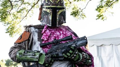 Bounty hunter in detailed Star Wars cosplay with vibrant armor and rifle outdoors.