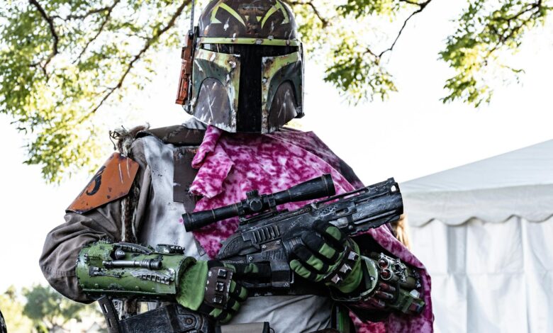 Bounty hunter in detailed Star Wars cosplay with vibrant armor and rifle outdoors.