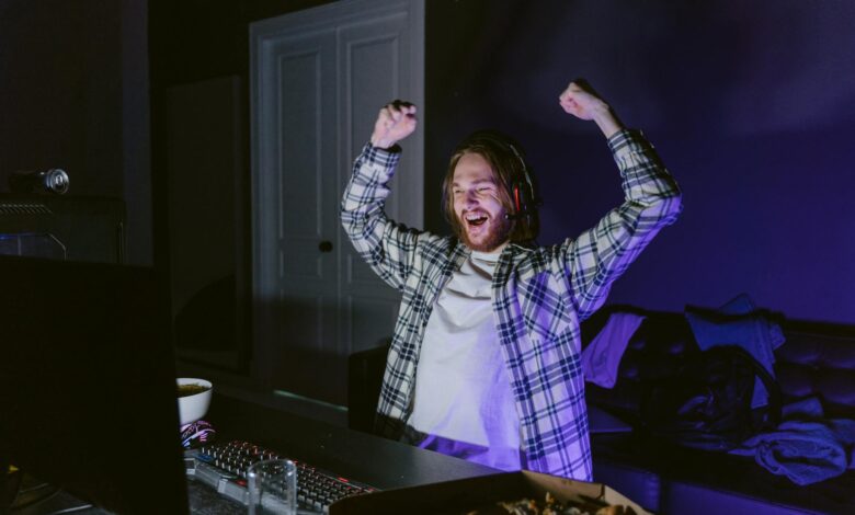 Joyful gamer celebrating victory while playing video games at night, wearing headphones.