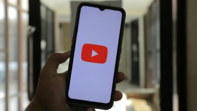 Close-up of a hand holding a smartphone displaying the YouTube logo in a well-lit room.