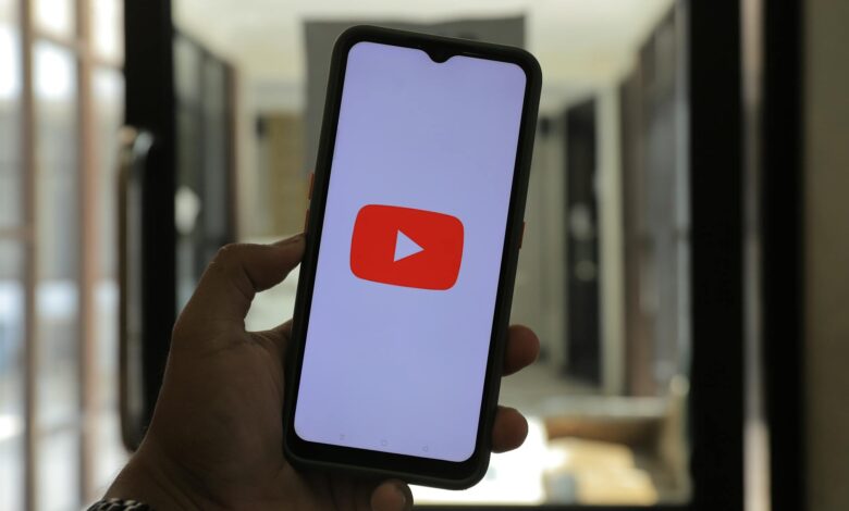 Close-up of a hand holding a smartphone displaying the YouTube logo in a well-lit room.