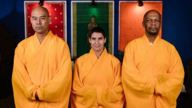 Three Buddhist monks in orange robes pose indoors promoting peace and mindfulness.