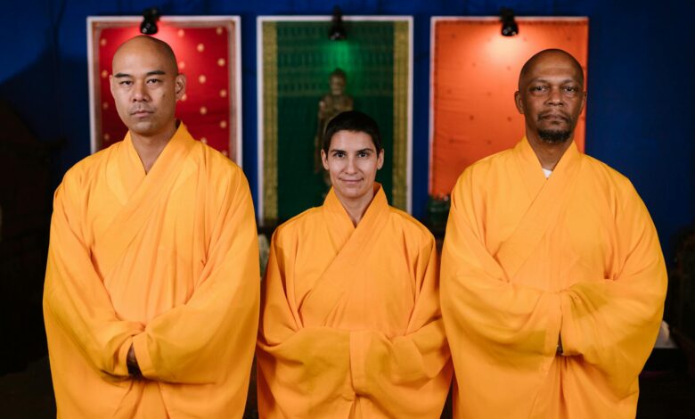 Three Buddhist monks in orange robes pose indoors promoting peace and mindfulness.
